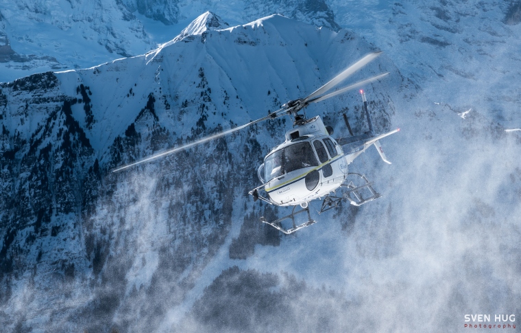 helicopter flying between snow-covered peaks